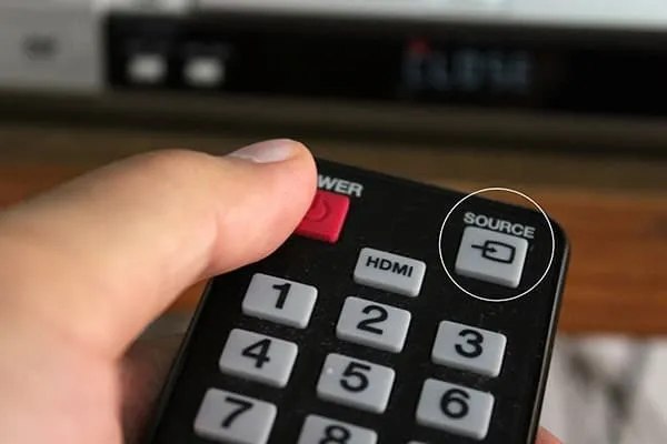 Hình ảnh người dùng đang sử dụng remote tivi để điều chỉnh cài đặt hiển thị, một bước quan trọng trong cách biến tivi thành máy tính