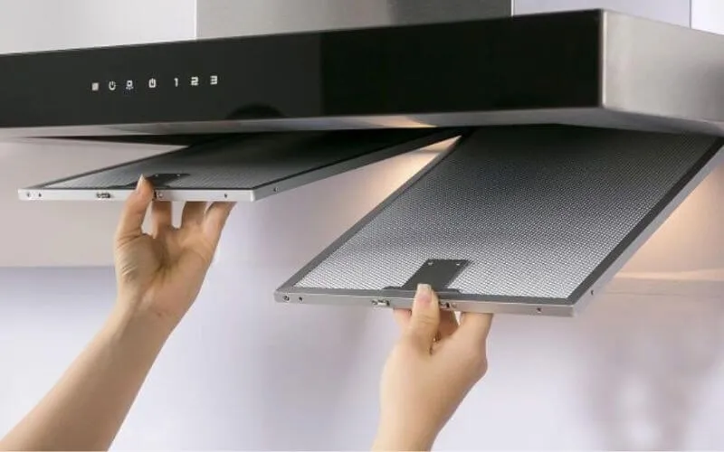 Thao tác nhấn lẫy cài để tháo màng lọc mỡ kim loại của máy hút mùi than hoạt tính